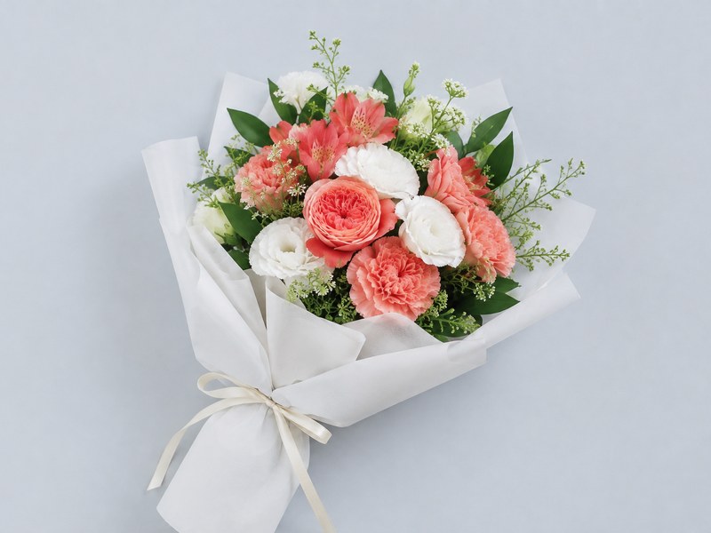 明るい青みがかったグレーの背景に、白い紙で包まれた花束が置かれているところ